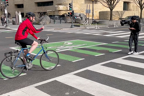 cyclist and a pedestrian in a crosswalk both on cellphones