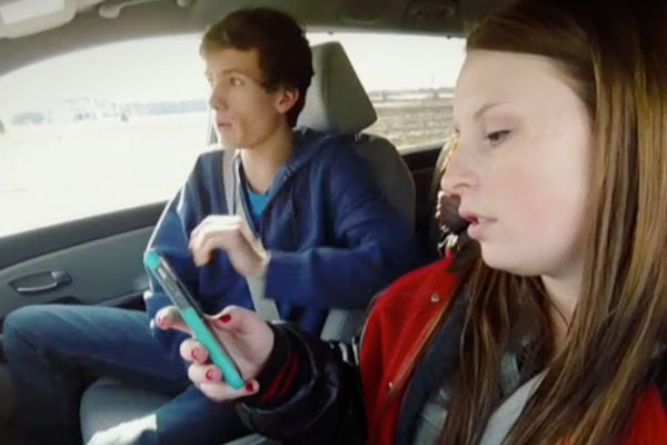 close up of teens in a car, with the girl behind the wheel texting