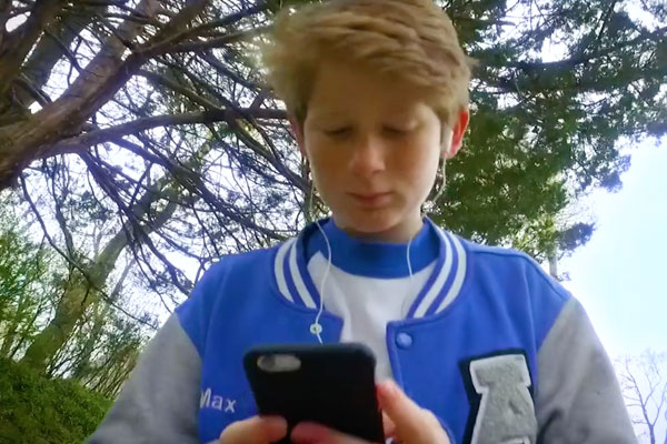a young boy with ear buds in and looking down at his phone