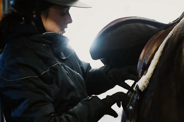 a girl adjusting a saddle on a horse